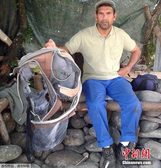 圖為當(dāng)?shù)貢r間7月30日，留尼旺島上的一名海岸清潔人員展示他找到的一個手提箱的殘骸。